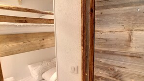 Une chambre avec un lit superposé, des poutres en bois et un mur blanc.