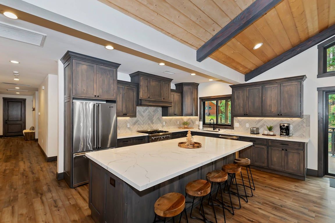 A modern kitchen with a large island, dark wood cabinets, stainless steel appliances, and a herringbone tile backsplash.