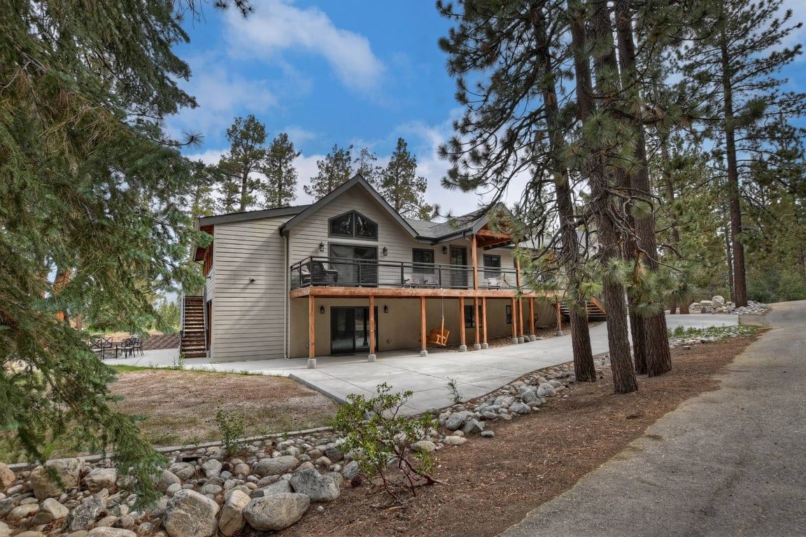 A two-story house with a balcony, surrounded by trees and a stone pathway.