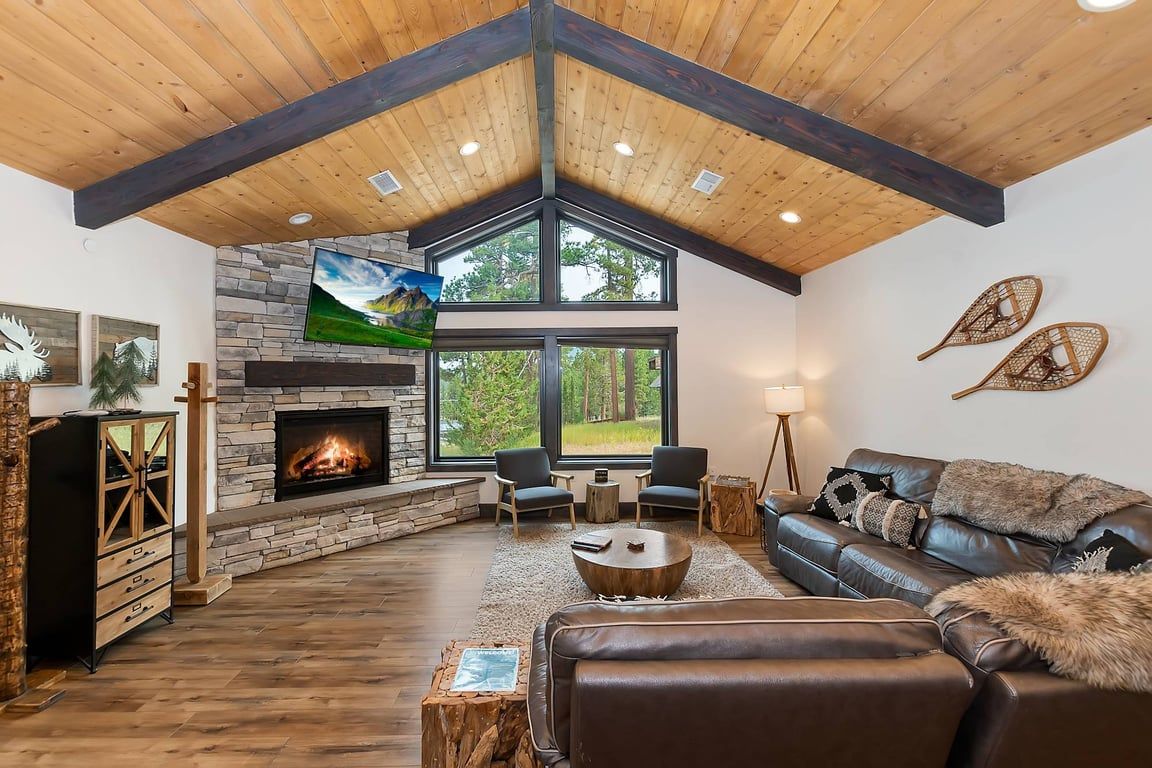 A modern living room with a stone fireplace, leather sofa, and a large window offering a view of the outdoors.