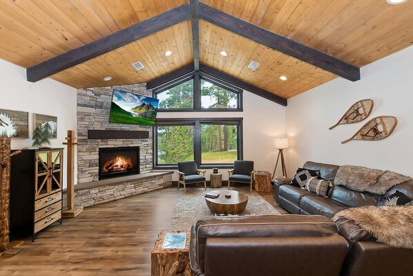 A modern living room with a stone fireplace, leather sofa, and a large window offering a view of the outdoors.