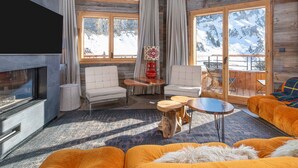 Un salon chaleureux avec une cheminée, des fauteuils confortables et de grandes fenêtres donnant sur un paysage de montagnes enneigées.