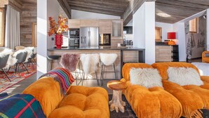 Un salon moderne avec un grand canapé orange, un plafond en bois et une cuisine en arrière-plan.