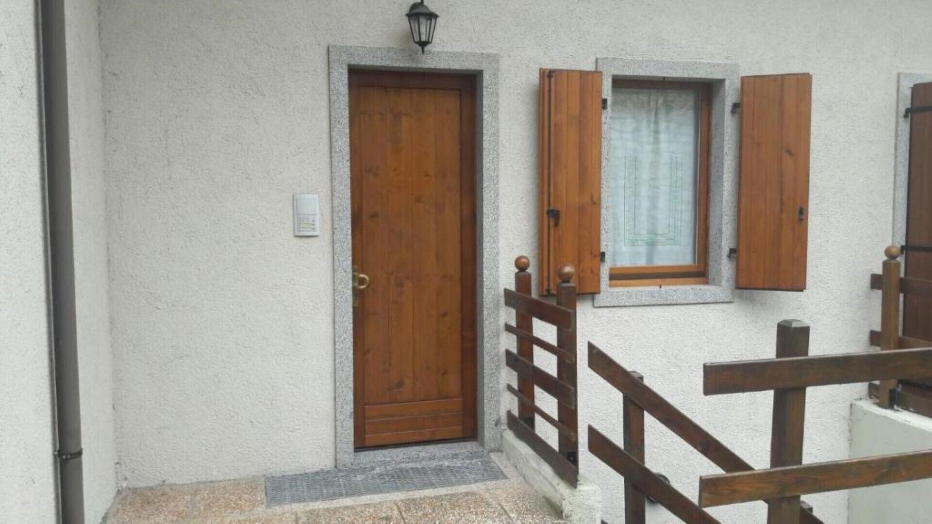 Un edificio con una porta in legno, una piccola finestra con persiane e una ringhiera in legno.