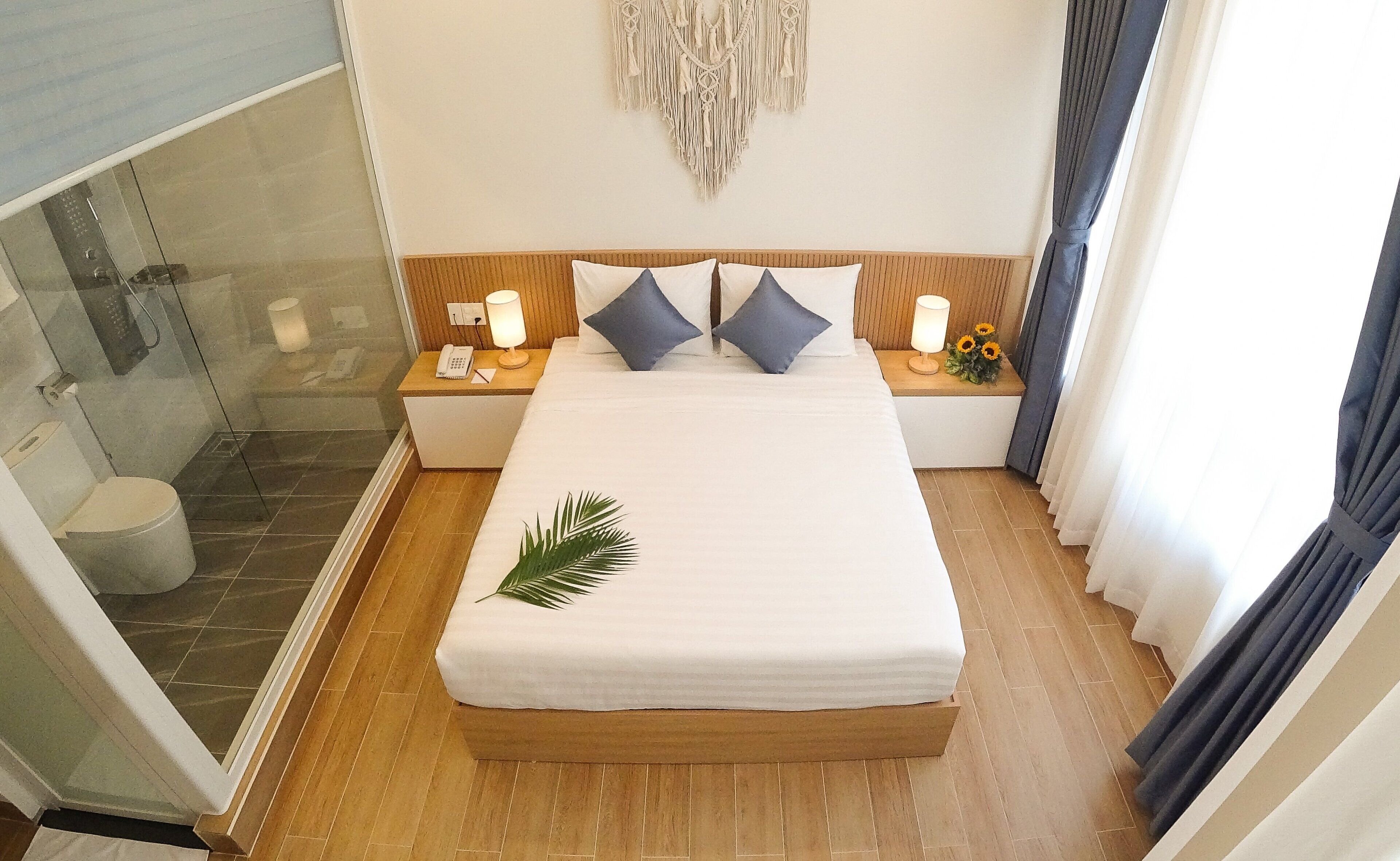 A hotel room with a bed, a bedside table with a lamp, a wall decoration, and a view of the outside.
