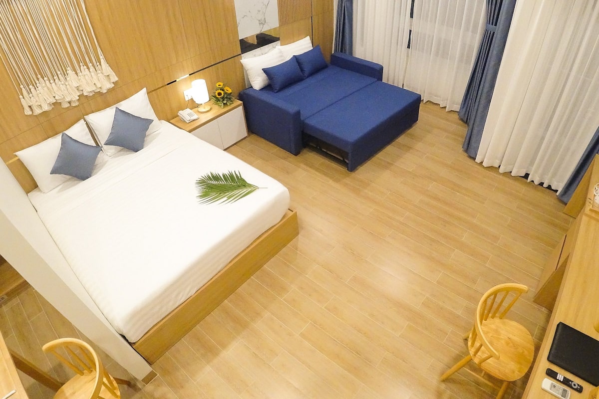 A hotel room with a bed, a sofa, a wooden nightstand with a lamp, and a chair.