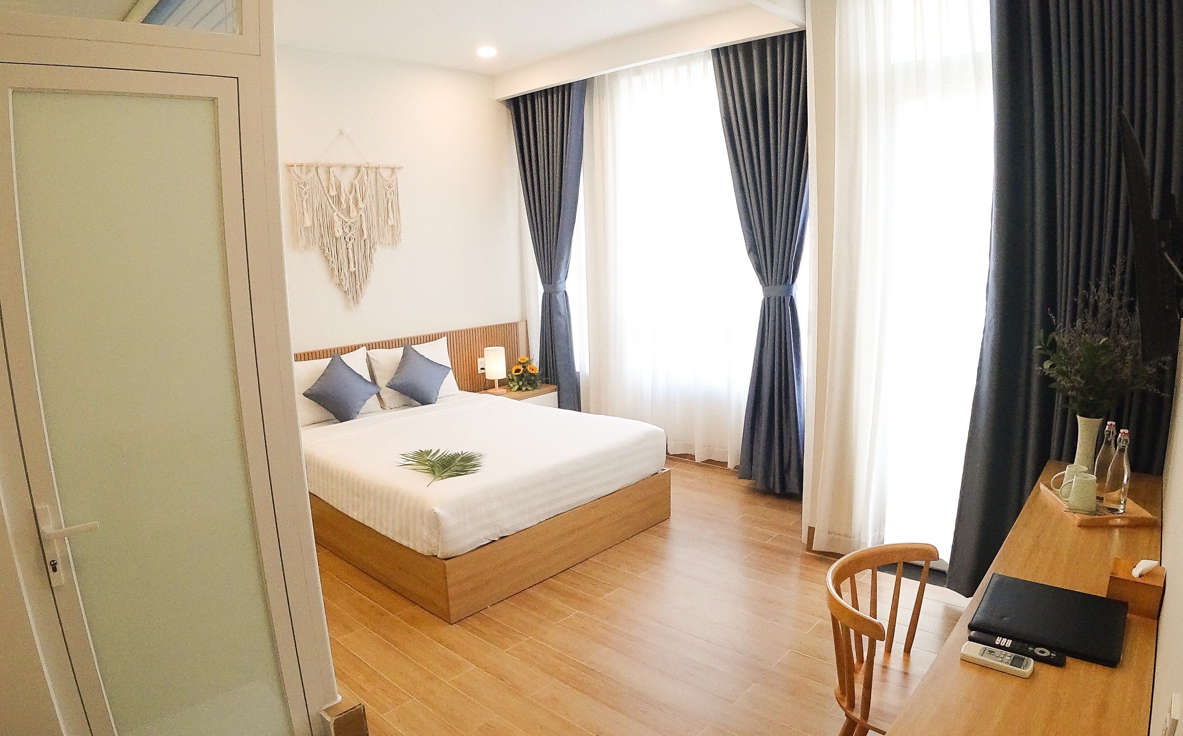 A bedroom with a wooden bed, a bedside table with a lamp, a chair, and a desk with a computer and a phone.
