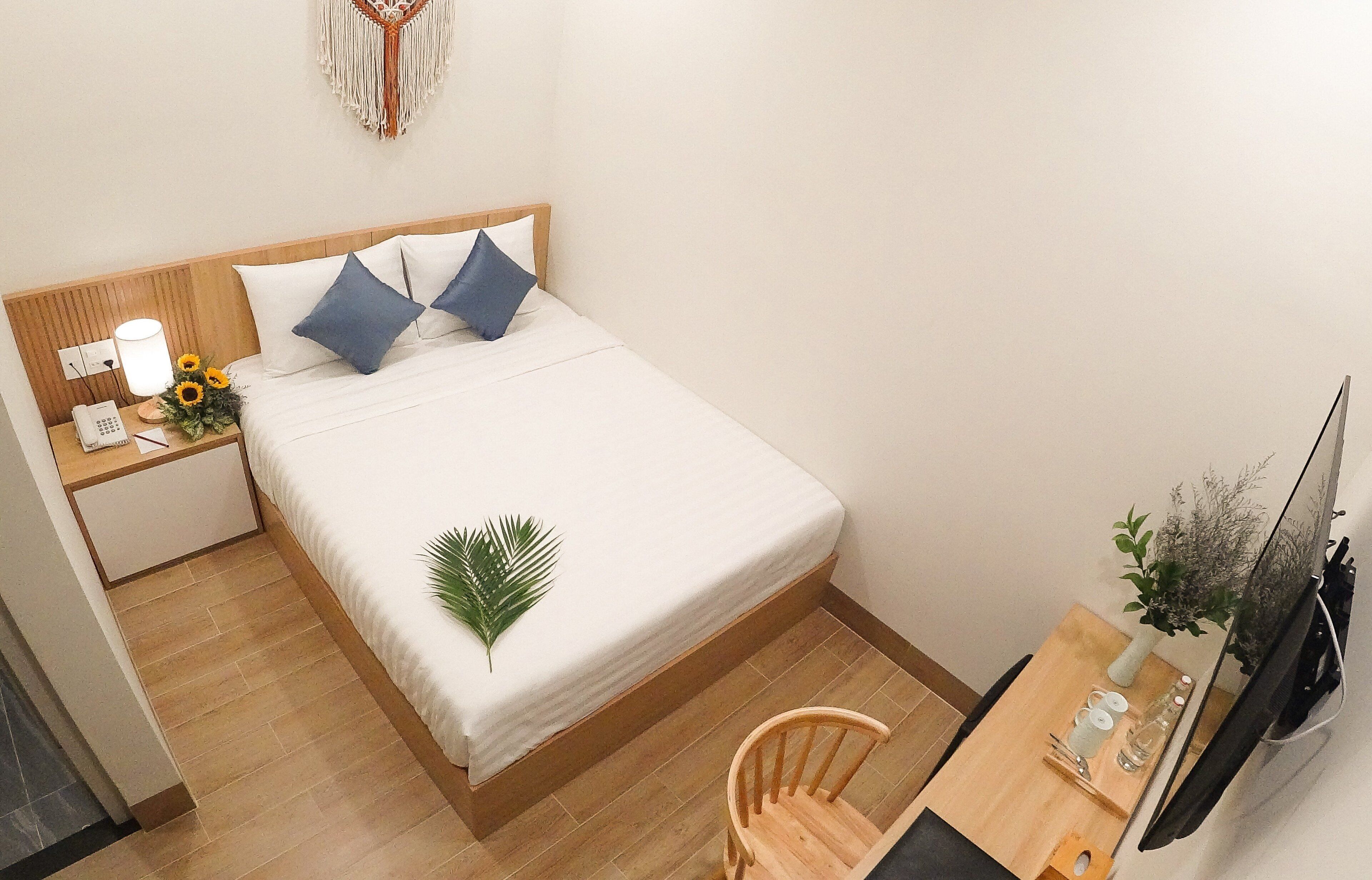 A neatly arranged hotel room with a bed, bedside table, lamp, phone, and a small desk with a chair.