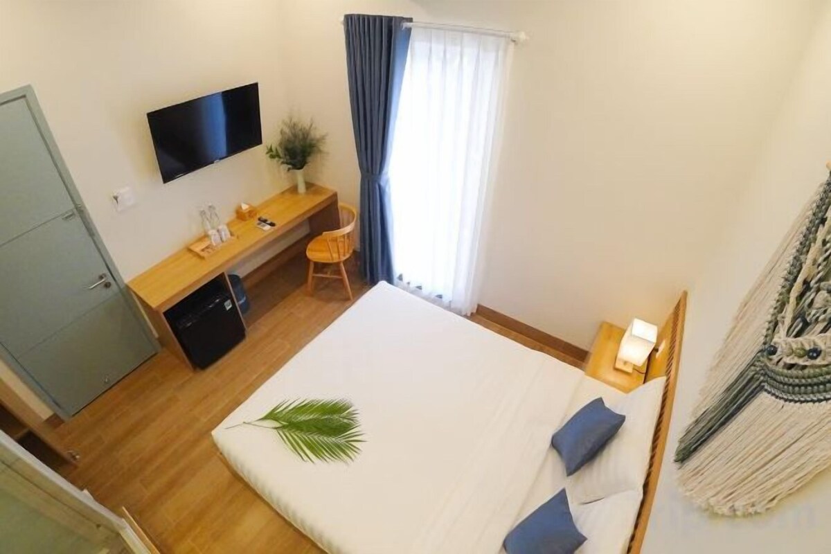 A bedroom with a bed, a desk, a TV, and a window with curtains.