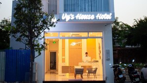 A modern hotel building with a flat facade, multiple balconies with plants, and a well-lit entrance. - Vy's House Phanthiet Hotel (Phu Thuy)