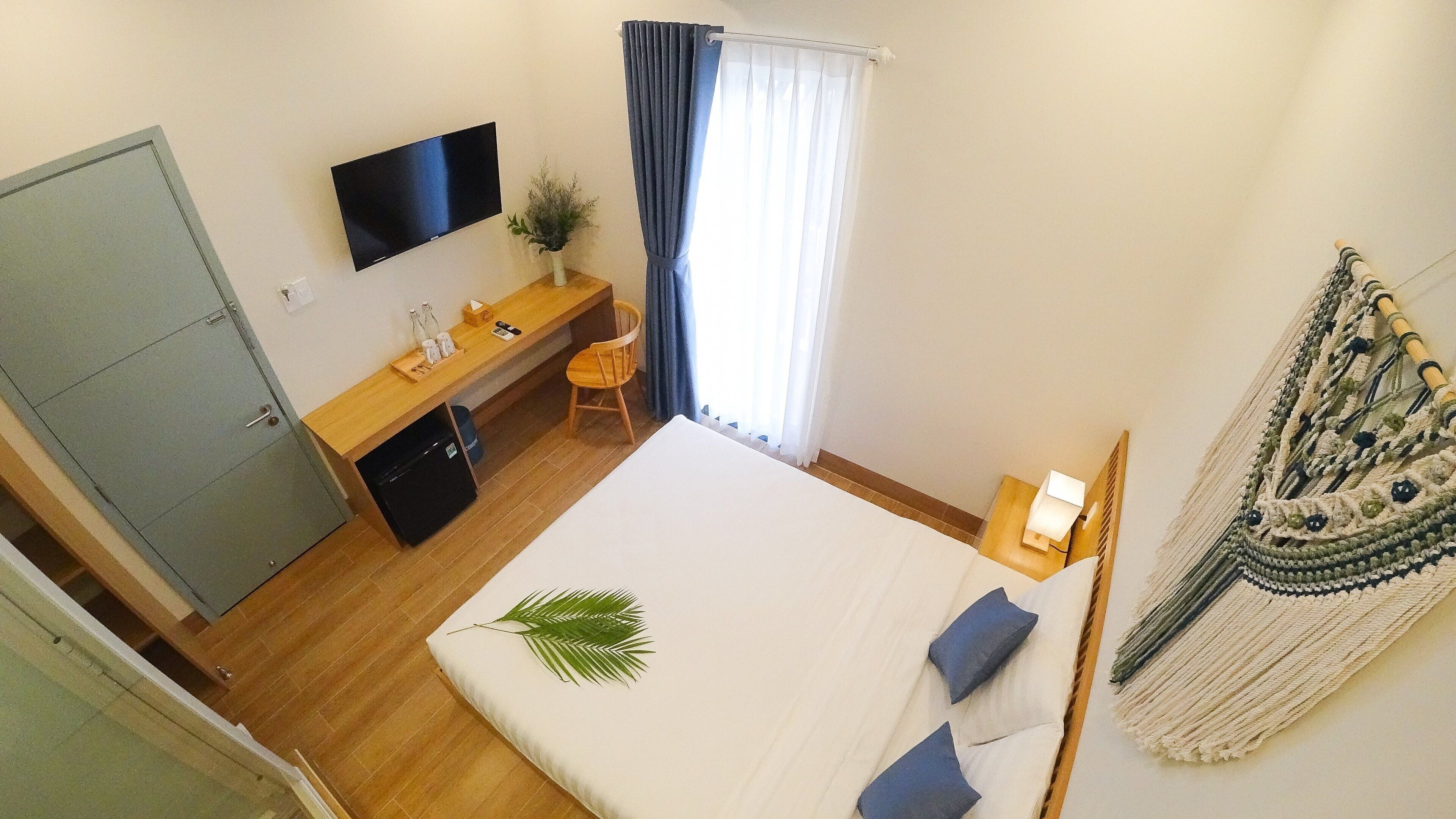 Un dormitorio con cama, escritorio, televisor, armario y ventana con cortinas.