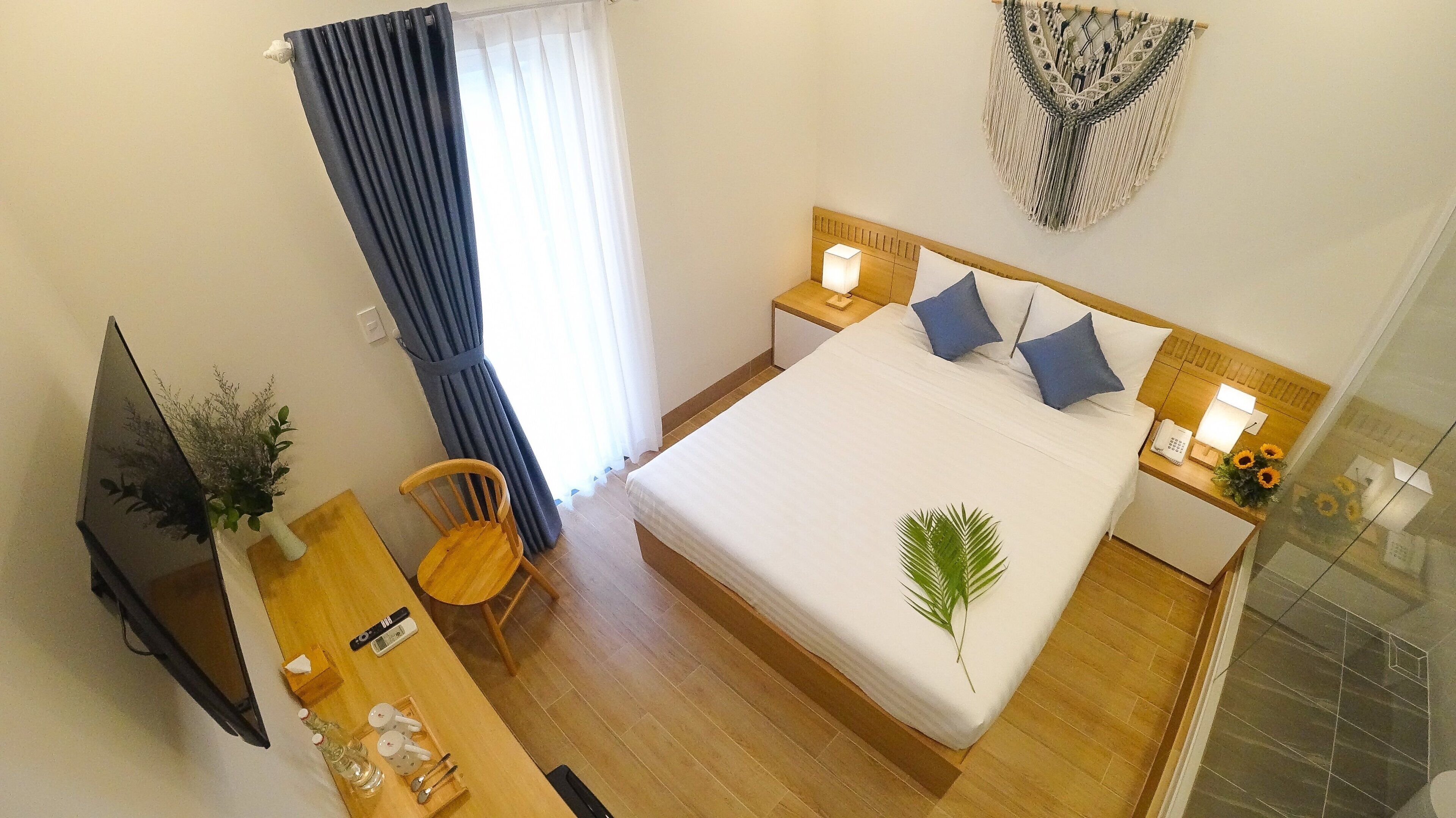 Una camera d'albergo con un letto, comodini, una scrivania con una sedia, una TV e un pannello decorativo in macramè.