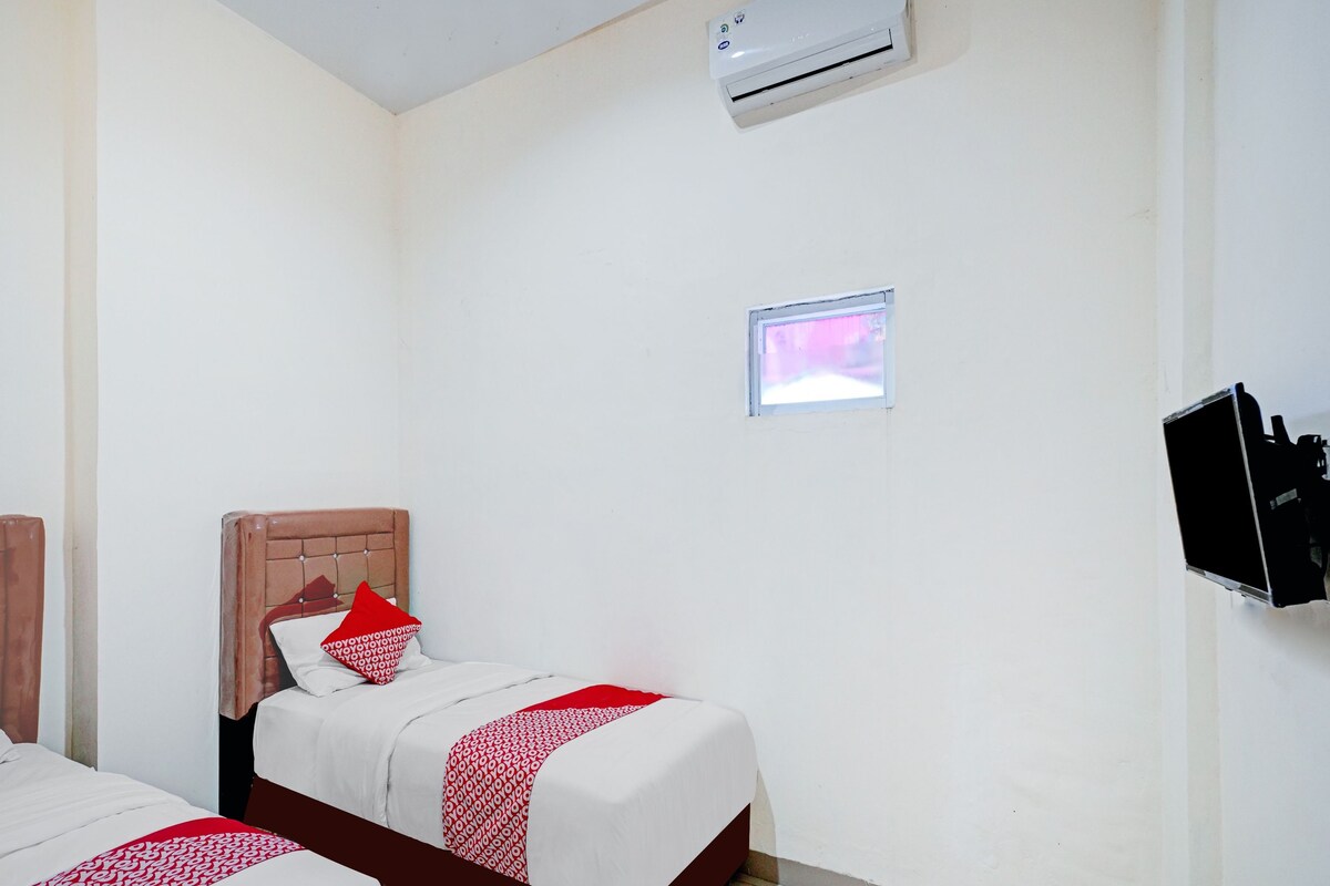 A hotel room with two beds, a TV, an air conditioner, and a small window.