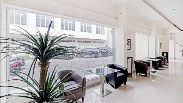 A modern hotel lobby with a large window, a palm plant, and a seating area with a glass table and chairs. - Hotel O Stm Suite Near Amplas Bus Terminal (Medan)