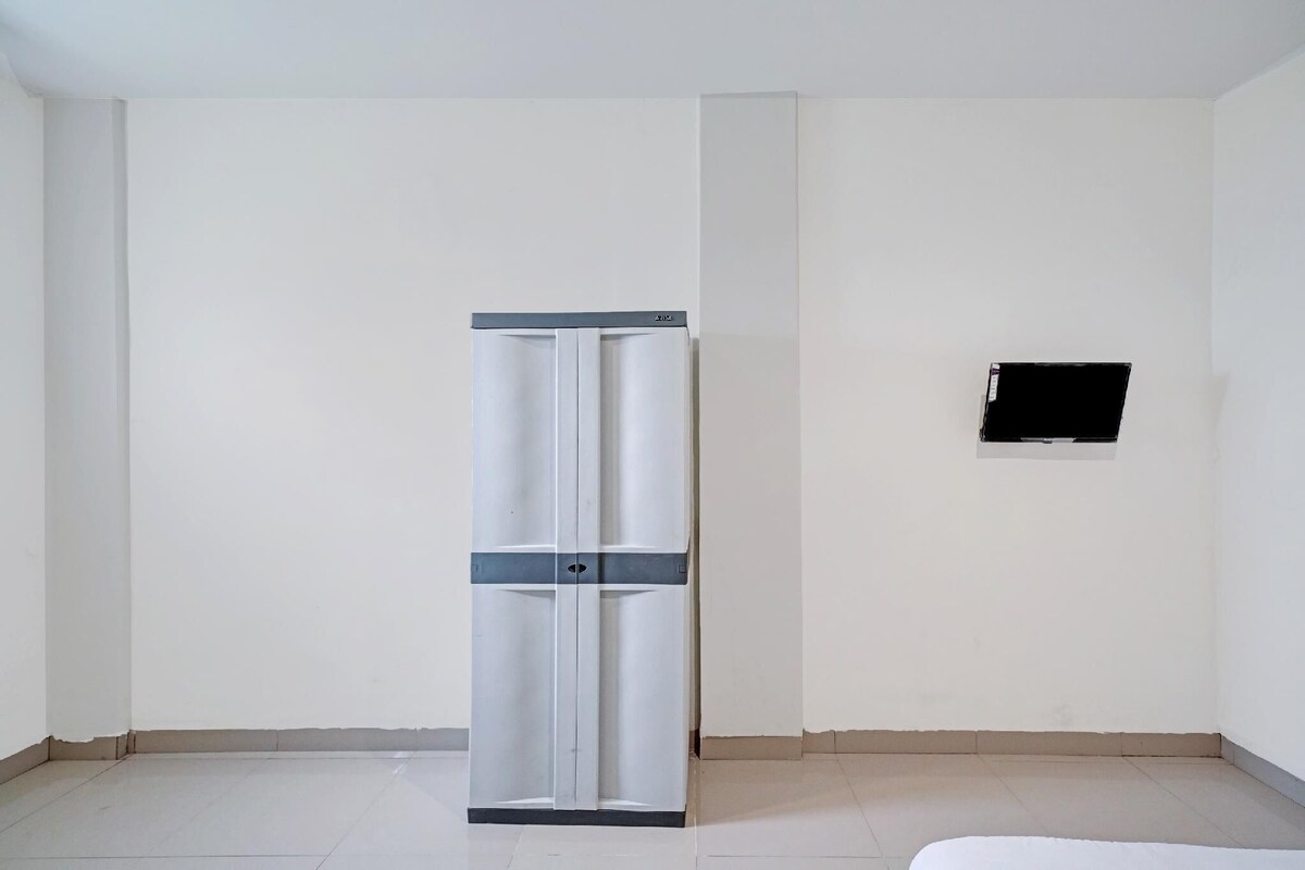 A room with a white wardrobe, a black TV mounted on the wall, and a tiled floor.