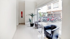 A modern hotel lobby with a large window, a potted plant, a sofa, and a small table. - Hotel O Stm Suite Near Amplas Bus Terminal (Medan)