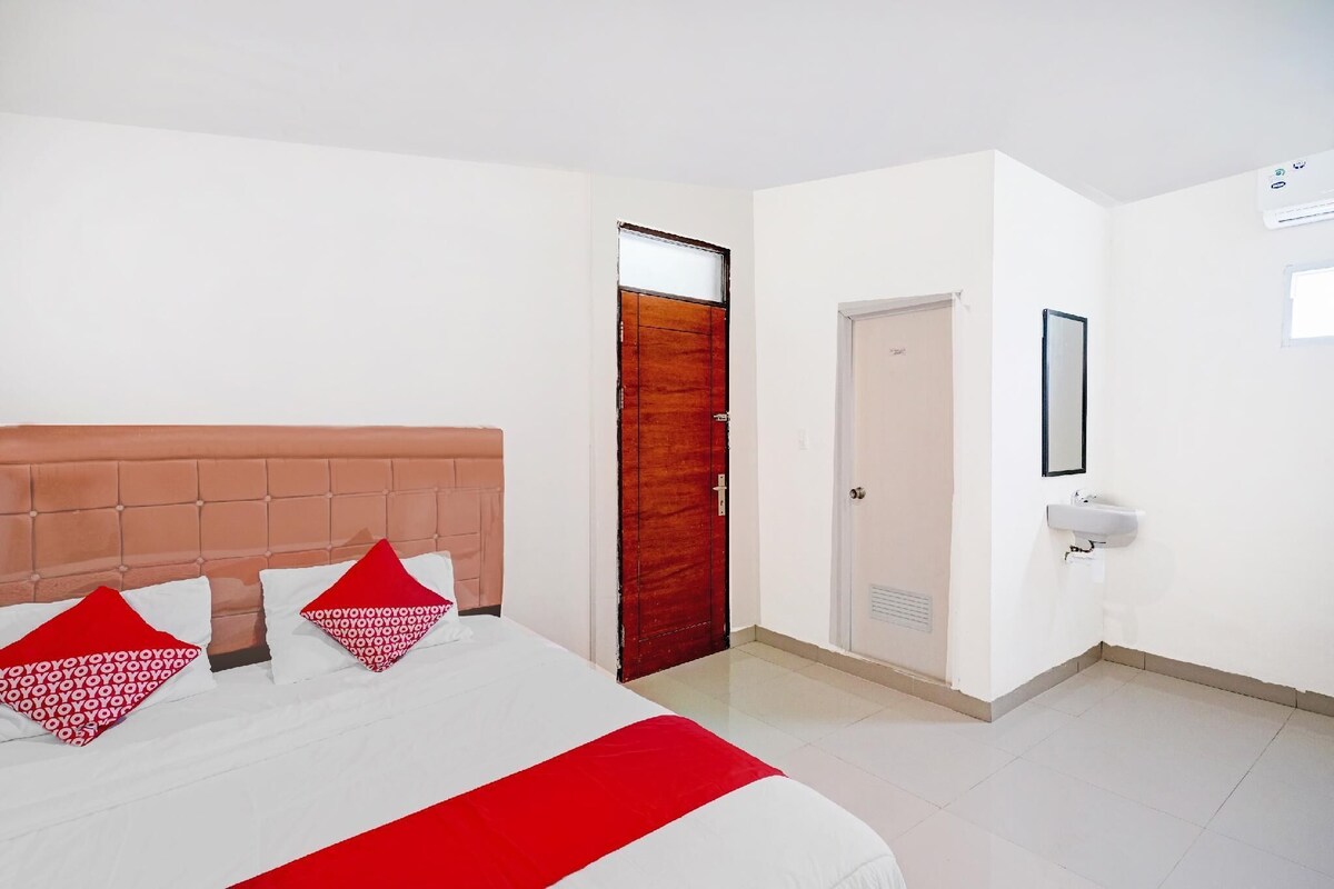 A hotel room with a bed, a wooden door, a white wall, a sink, and a mirror.