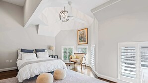 Une chambre à coucher avec un lit, une chaise, une fenêtre et un ventilateur de plafond.