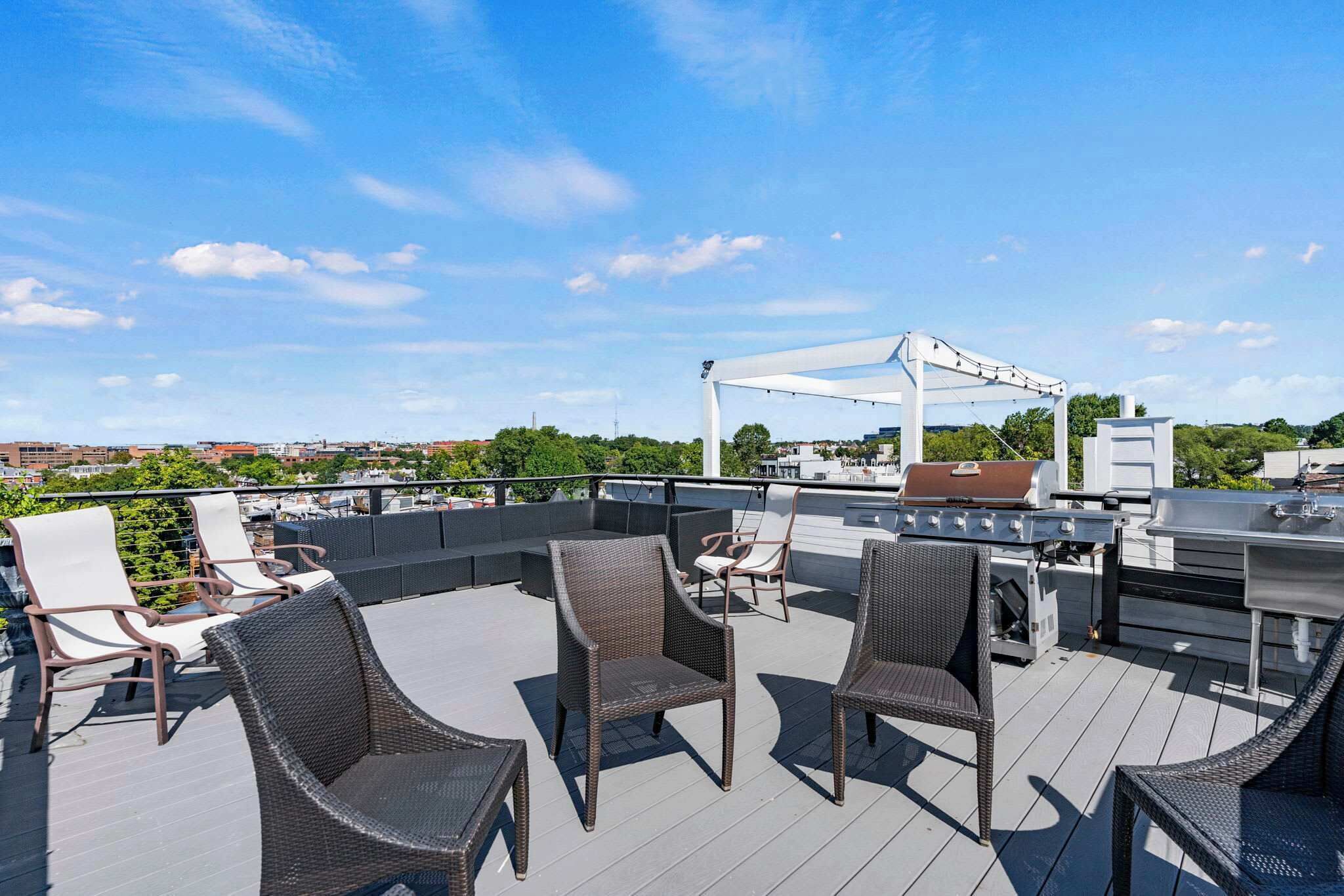 A rooftop deck with wicker furniture, a grill, and a pergola.