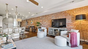 Un salon moderne avec un mur en briques, des meubles blancs, un téléviseur à écran plat et des luminaires suspendus.