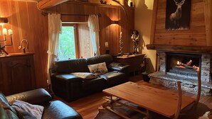A cozy living room with a fireplace, leather sofa, wooden coffee table, and a stone fireplace surround. - Chalet Luxueux à 500 Mètres des Pistes Avec Terrasse Plein sud (Saint-Véran)