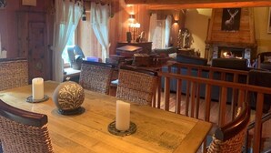 A cozy cabin interior with a dining table set for two, a fireplace, and wicker furniture. - Chalet Luxueux à 500 Mètres des Pistes Avec Terrasse Plein sud (Saint-Véran)