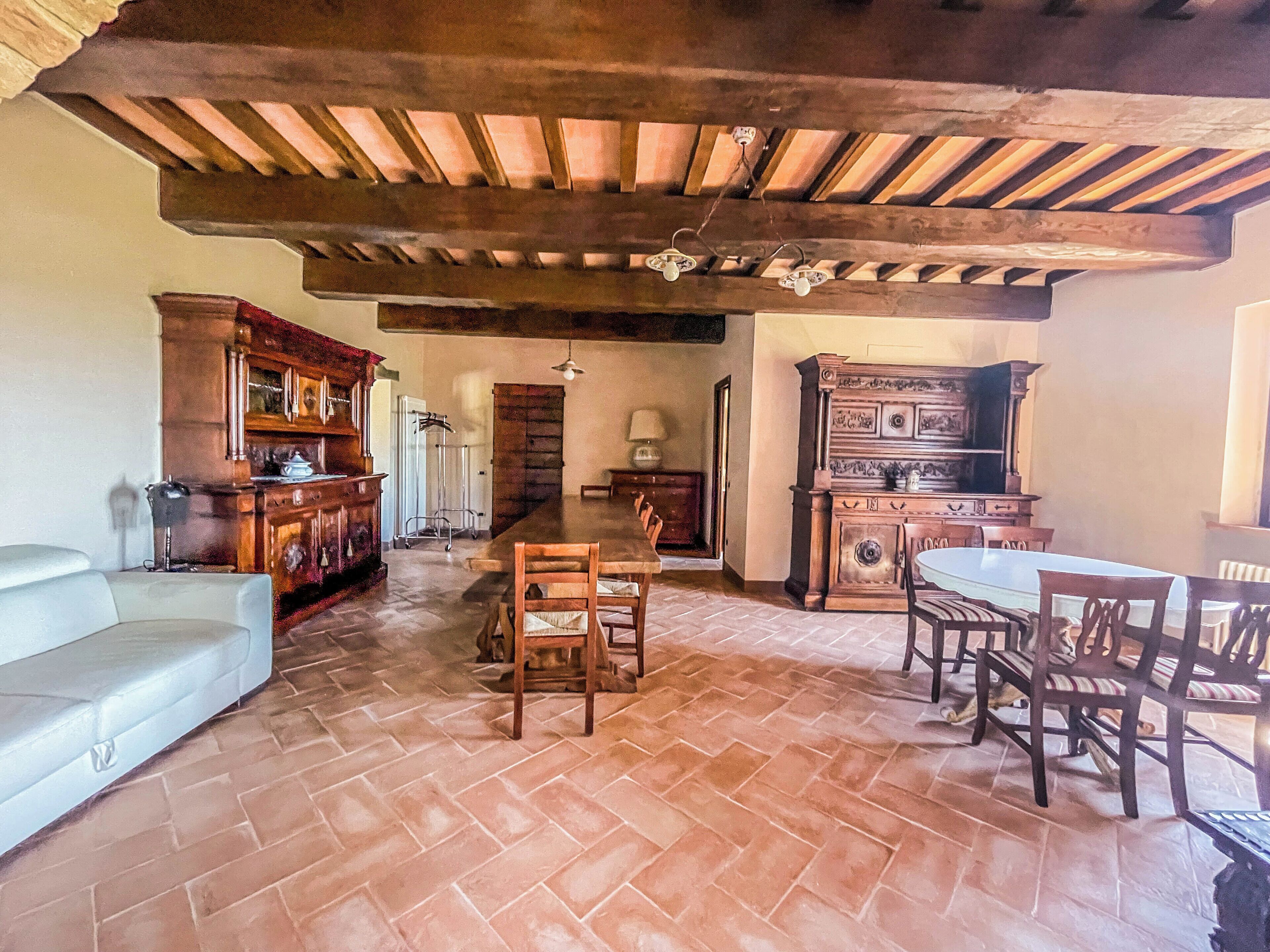A spacious room with a tiled floor, wooden furniture, and a high ceiling with exposed beams.