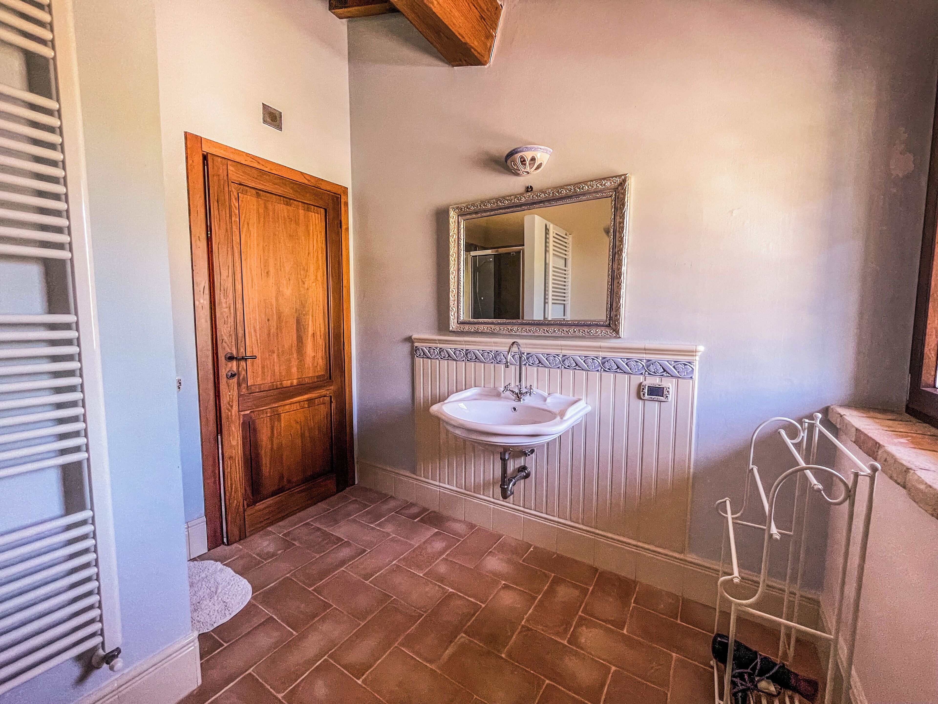 A bathroom with a wooden door, a white sink with a mirror above it, and a radiator on the wall.