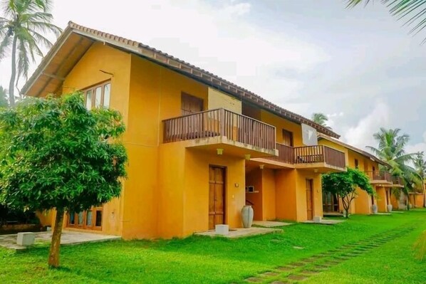 A yellow building with multiple balconies and a well-maintained lawn. - Muthumuni Ayurveda Beach Resort (Beruwala)