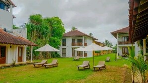 Een resort met meerdere villa's, elk met een balkon en een gazon. Er staan verschillende ligbedden en parasols in de binnenplaats.