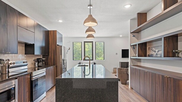 A modern kitchen with dark wood cabinets, stainless steel appliances, and a central island with a sink. - Tumbleweed -  Walk to Coffee + Dining + Garage (Shawnee)