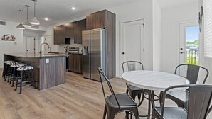 A modern kitchen with a central island, stainless steel appliances, and a dining area with a round table and chairs. - Tumbleweed -  Walk to Coffee + Dining + Garage (Shawnee)