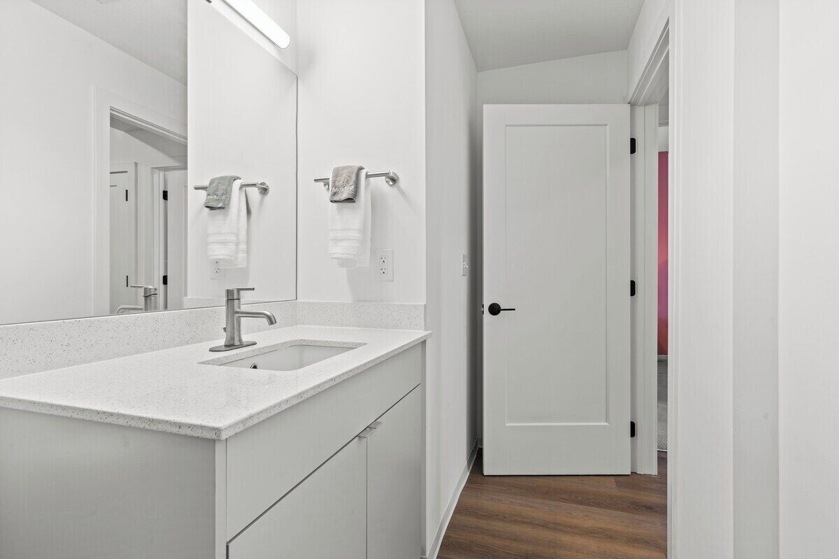 Un bagno con lavandino bianco, specchio e porta asciugamani.