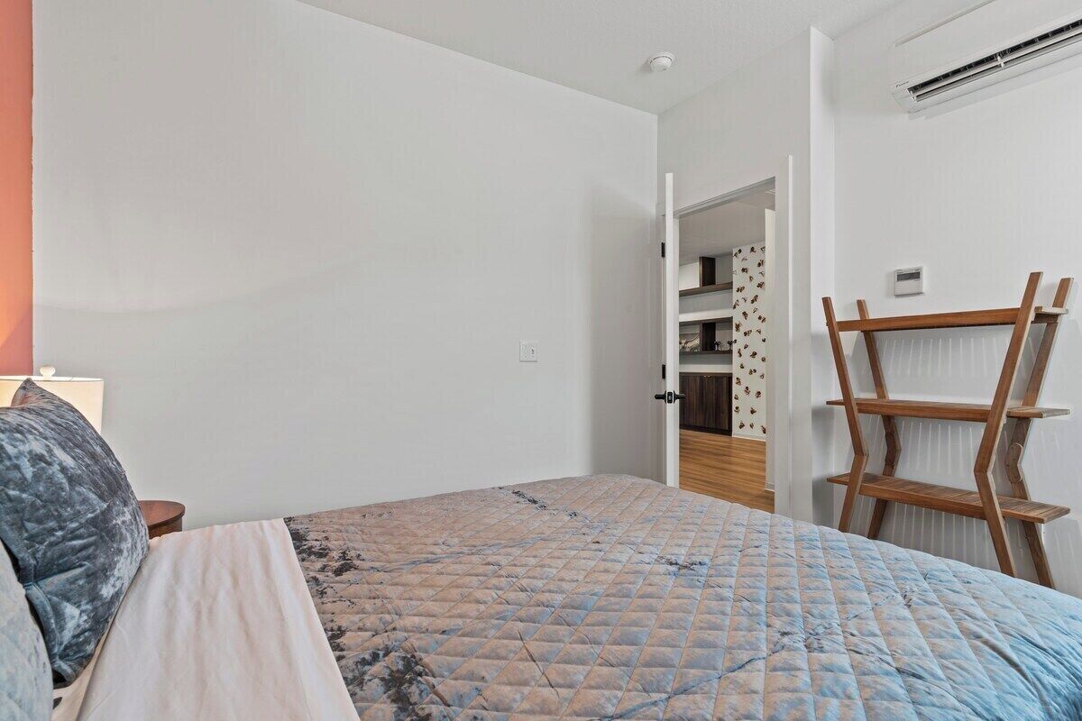A bedroom with a bed, a nightstand, a wooden ladder, and a door leading to a bathroom.