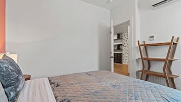 A bedroom with a bed, a nightstand, a wooden ladder, and a door leading to a bathroom.