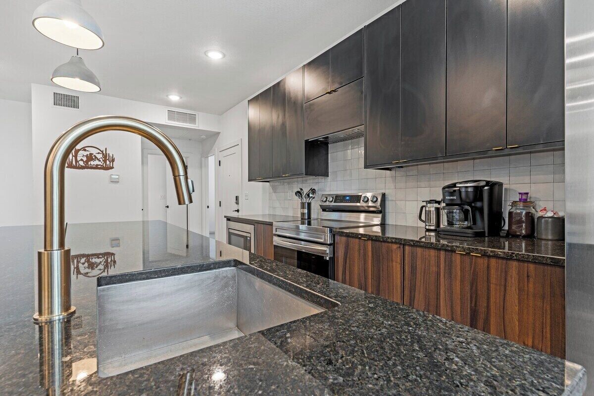 A modern kitchen with stainless steel appliances, a granite countertop, and dark wooden cabinets.