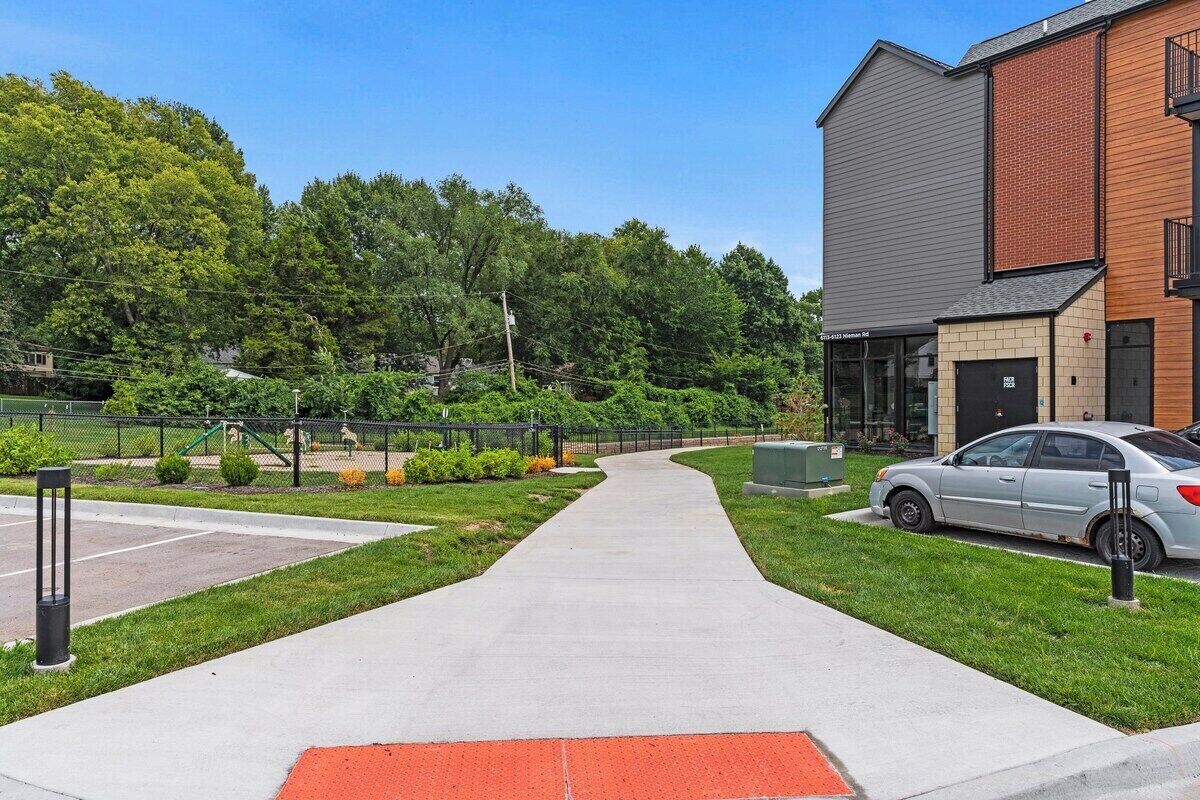 Un chemin menant à un bâtiment, avec un espace de stationnement et de la verdure en arrière-plan.