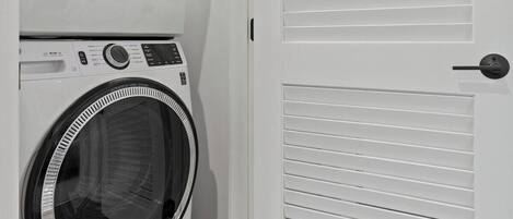 A laundry room with two front-loading washing machines and a white door with horizontal slats.
