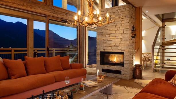A cozy living room with a fireplace, a sofa, a coffee table with chess, and a view of mountains. - Luxury chalet for 12 near slopes, with sauna (Saint-Martin-de-Belleville)