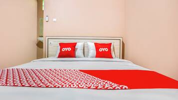 A bed with a red and white patterned blanket, two red pillows with "OYO" text, and a beige headboard.