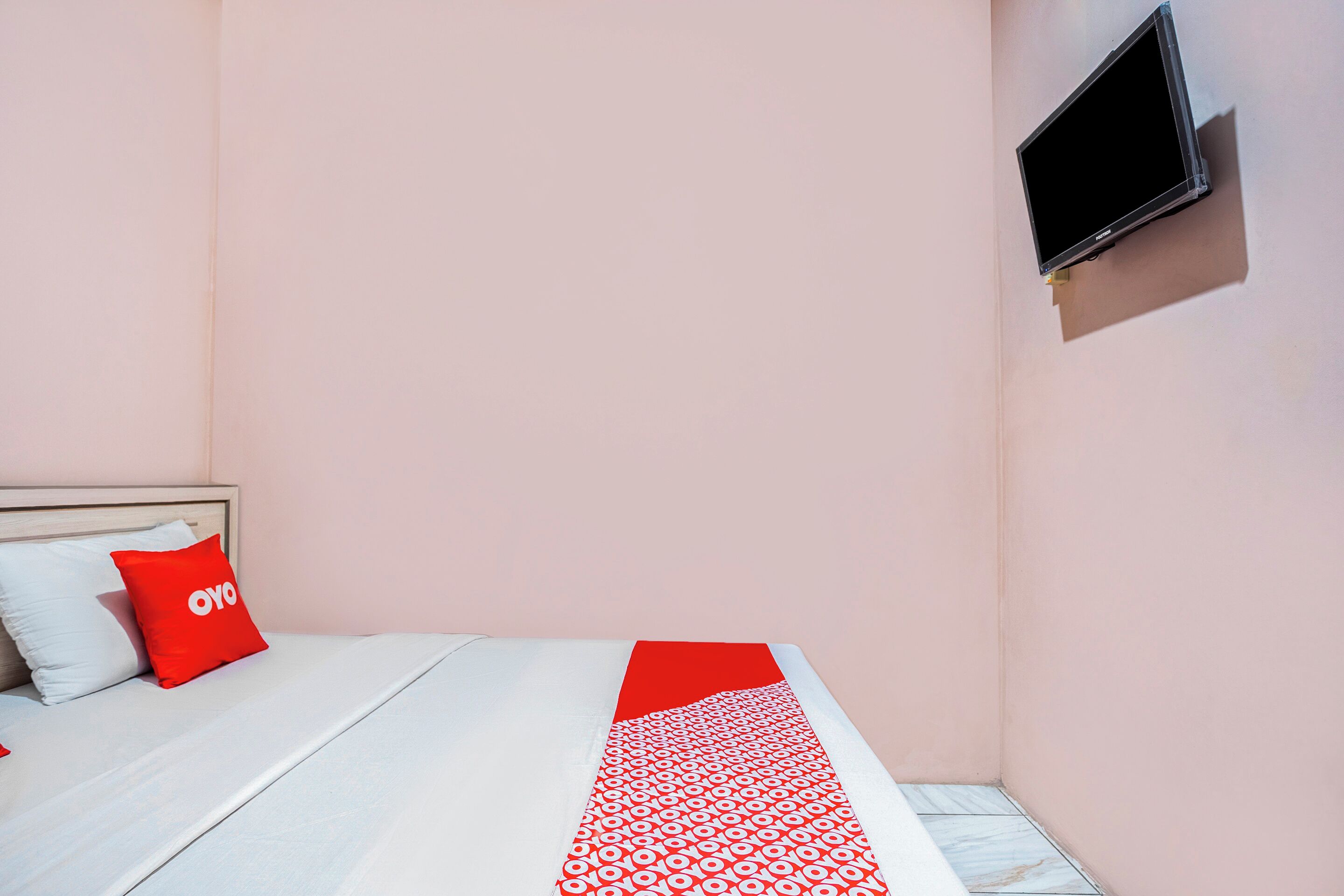 A bedroom with a bed, a red and white patterned bedspread, a red pillow with the word "oyo", and a TV mounted on the wall.
