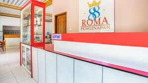 Una zona de recepció amb un senyal que diu "RECEPTIONIST" i un logotip de "ROMA PENGINAPAN" a la paret.