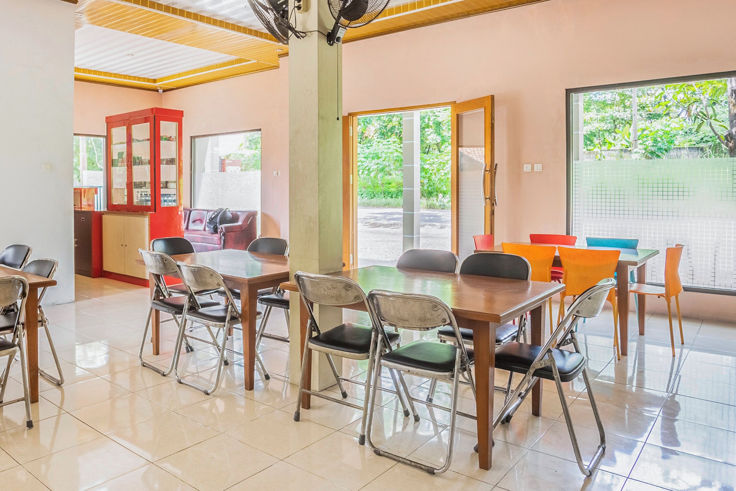 A dining area with a long table and chairs, a cabinet with glass doors, and a view of greenery outside.