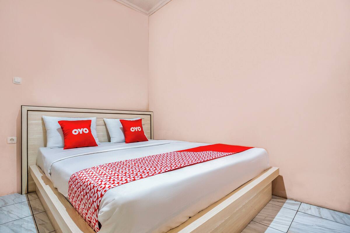 A neatly made bed with a white and red patterned bedspread, two red pillows with the word "OYO" on them, and a wooden headboard.