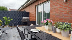 An outdoor patio with a table set for dining, a grill, and potted plants. - Tolle Ferienwohnung in Ruhiger Lage! (Eilsum)