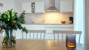 A modern kitchen with white cabinetry, a stainless steel range hood, and a dining area with a wooden table and chairs. - Tolle Ferienwohnung in Ruhiger Lage! (Eilsum)