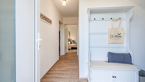 Un corridoio che conduce a una camera da letto con una panca bianca, una borsa appesa e un letto con cuscini.