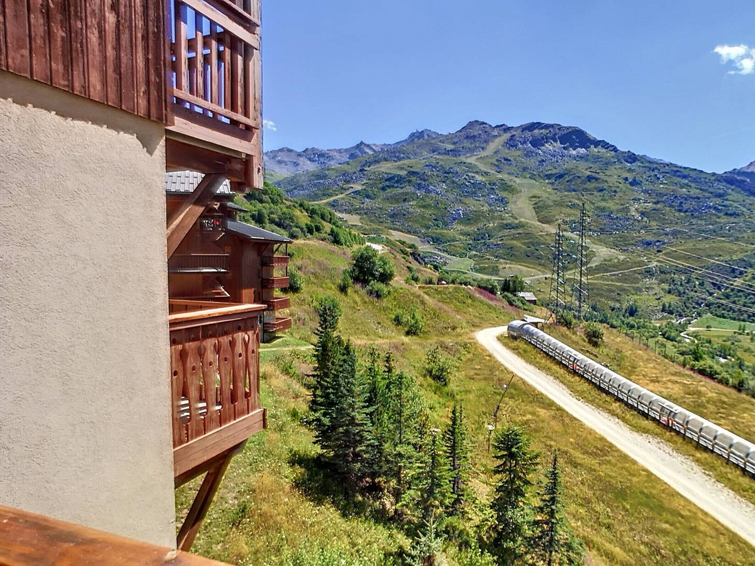 A wooden building with a balcony overlooking a mountainous landscape and a train on a nearby track.