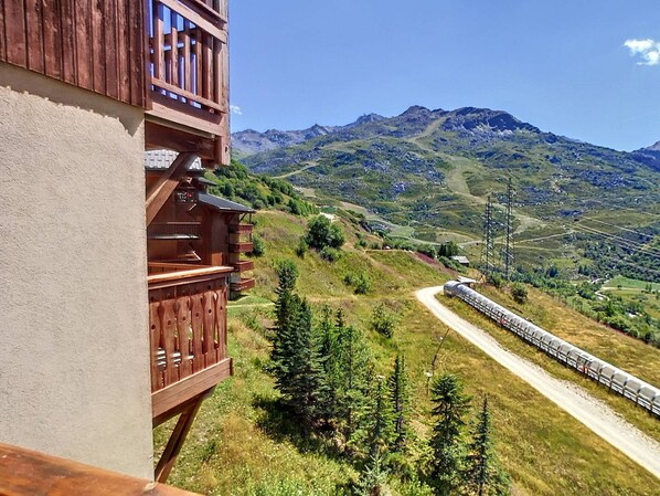 A wooden building with a balcony overlooking a mountainous landscape and a train on a nearby track.