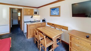 A compact kitchen with wooden cabinets, a microwave, and a sink. There's a dining table with chairs and a small wooden dresser. - Pleasant 2 rooms, 4 pers, south, Les Bruyères (Les Menuires)